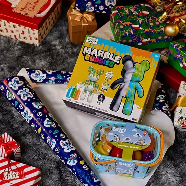 Children’s craft kit and toy shopping basket displayed amongst wrapped Christmas presents and festive gift wrap.